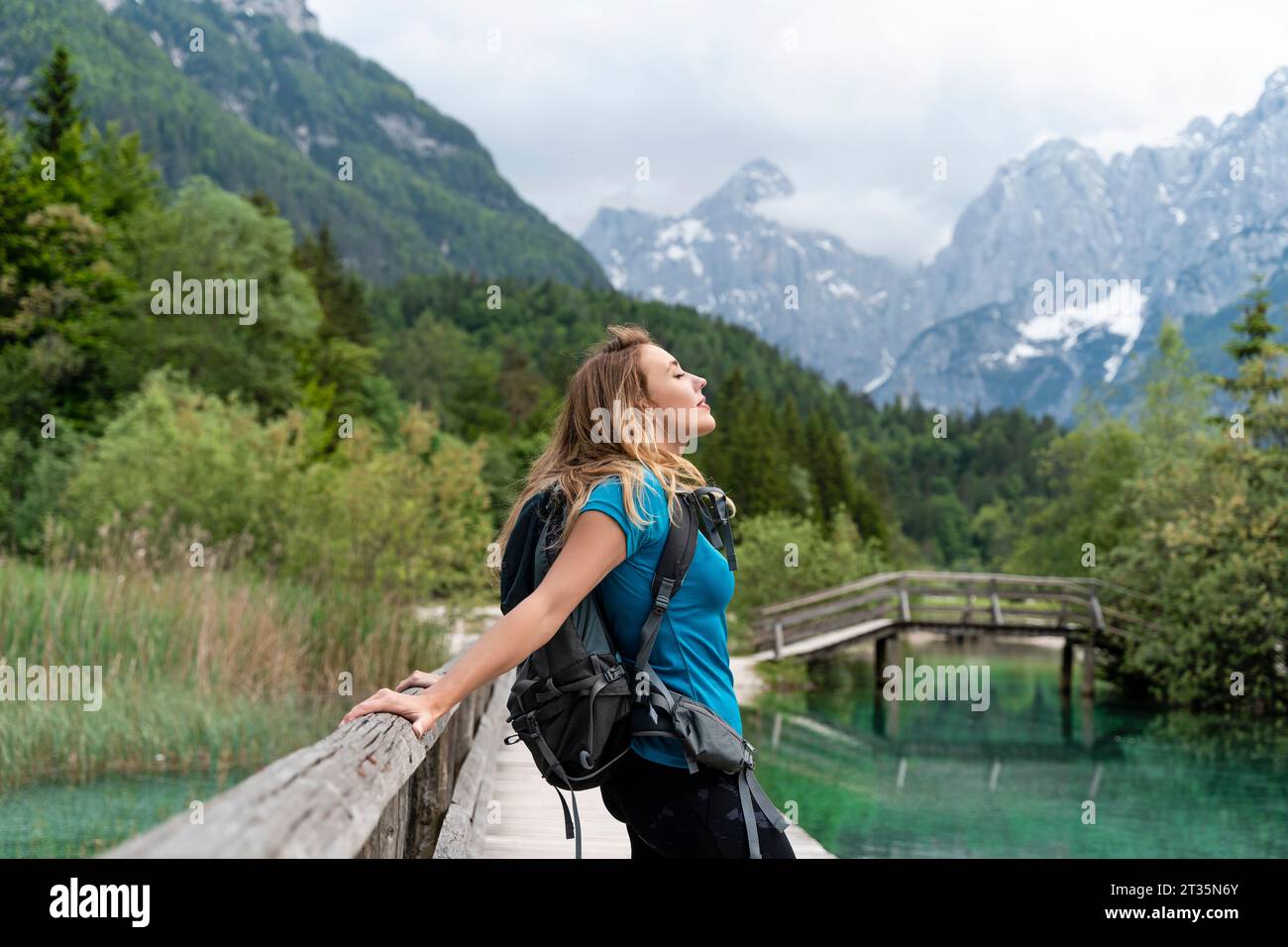 Backpacker con gli occhi chiusi rilassandosi sul molo vicino alle montagne Foto Stock