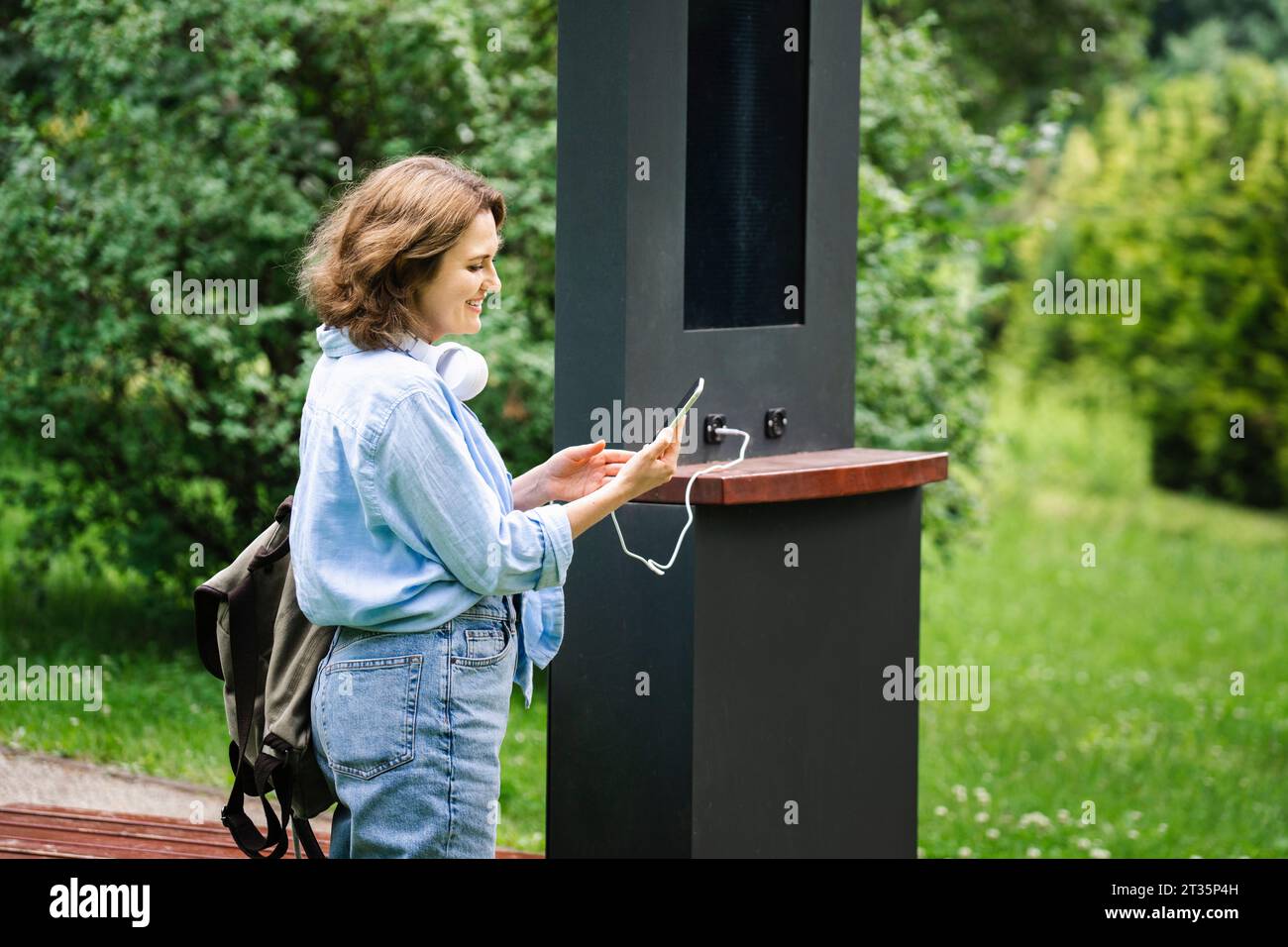 Donna sorridente che ricarica lo smartphone tramite l'energia solare al parco Foto Stock