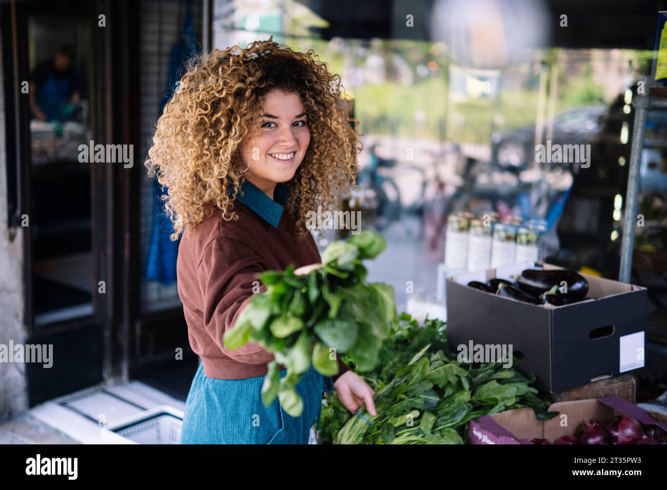 Donna d'affari sorridente che tiene verdure a foglia all'aperto Foto Stock
