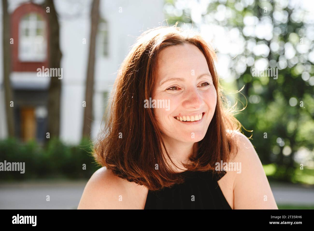 Donna felice con i capelli di media lunghezza sorridente nelle giornate di sole Foto Stock