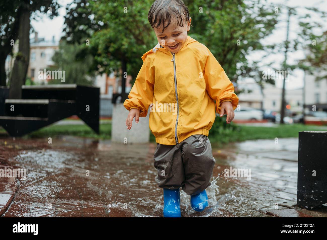 Happy boy che spruzza acqua in pozzanghera al parco Foto Stock