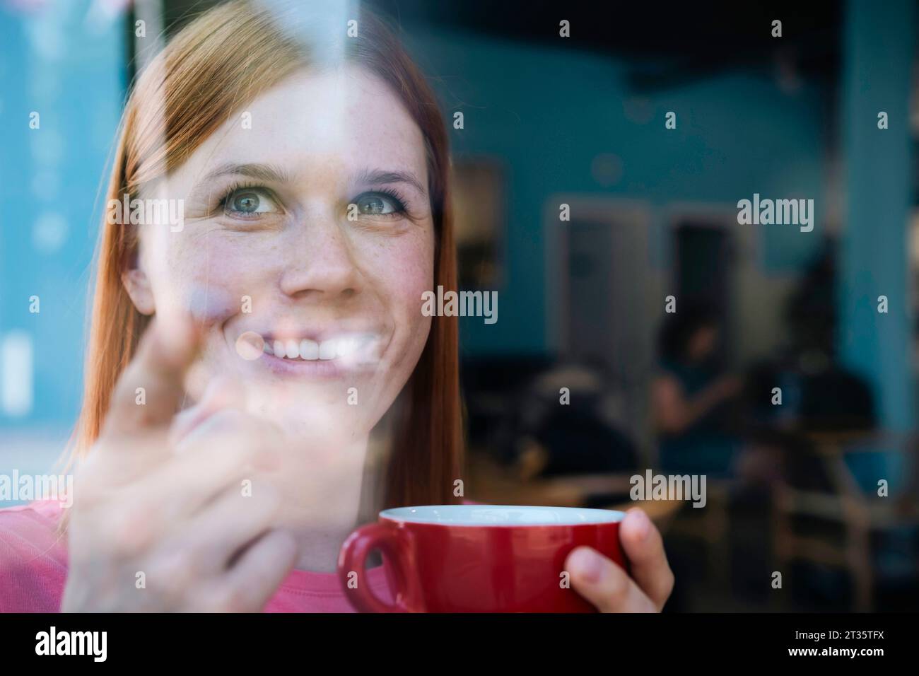 Donna sorridente che tiene una tazza di caffè al bar Foto Stock