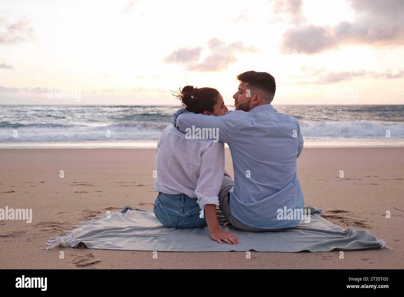 Un uomo con il braccio intorno a una donna seduta in spiaggia Foto Stock