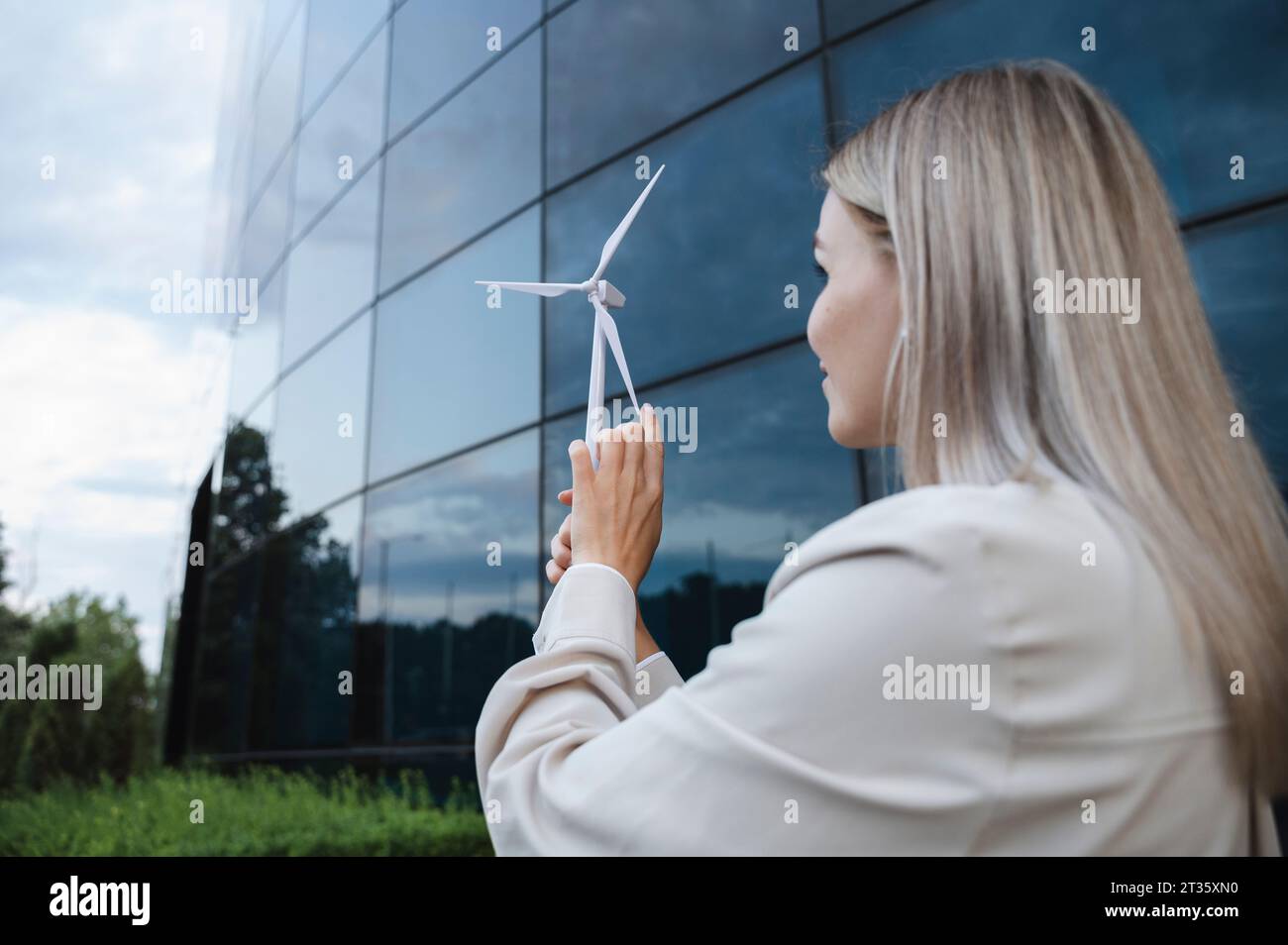 Donna d'affari che esamina il modello di turbina eolica di fronte all'edificio Foto Stock