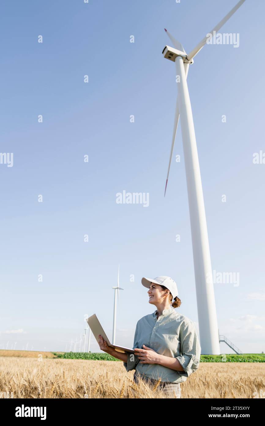 Agricoltore felice con un computer portatile davanti alle turbine eoliche nelle giornate di sole Foto Stock Agricoltore felice con un computer portatile davanti alle turbine eoliche nelle giornate di sole Foto Stock