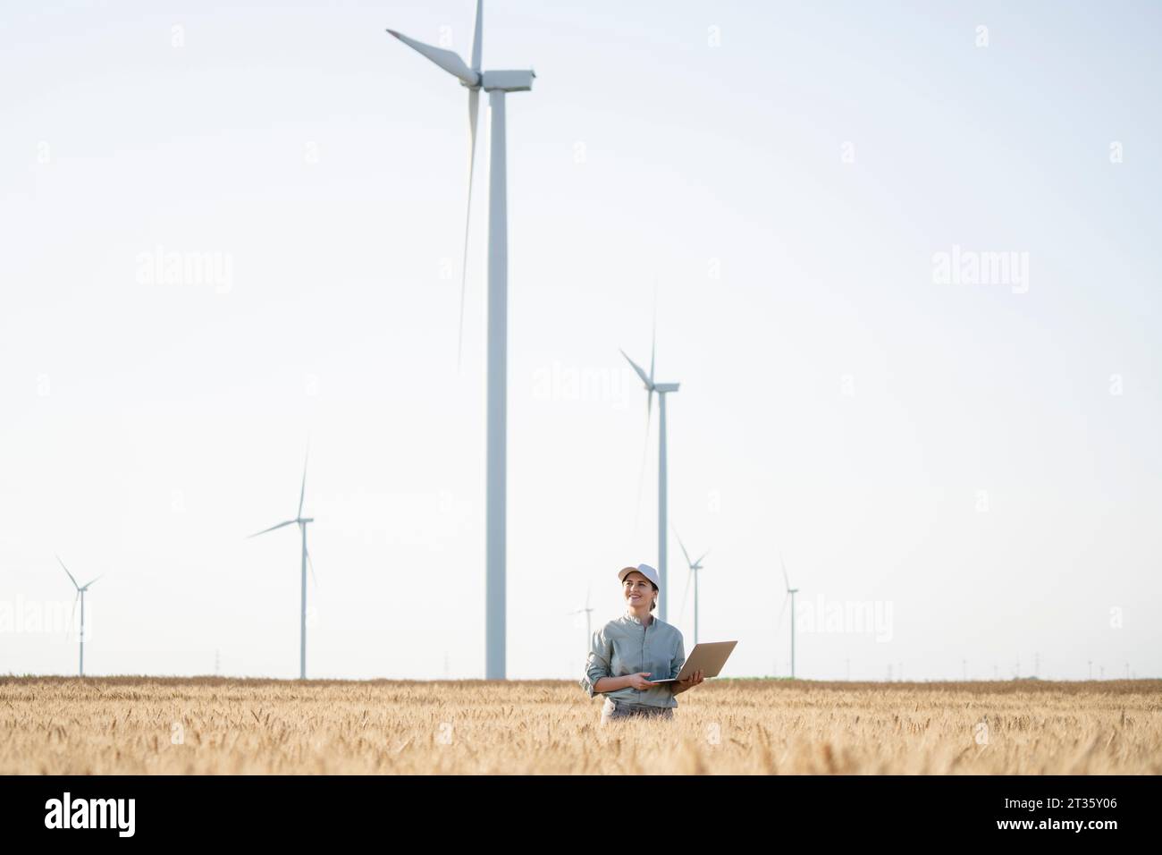 Donna d'affari felice in piedi con un computer portatile davanti alle turbine eoliche Foto Stock Donna d'affari felice in piedi con un computer portatile davanti alle turbine eoliche Foto Stock