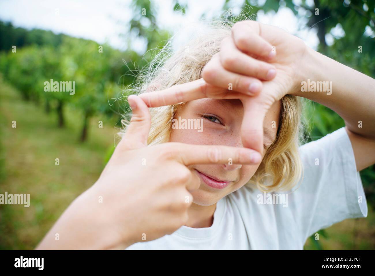 Ragazzo biondo che mostra un cartello con il dito in giardino Foto Stock