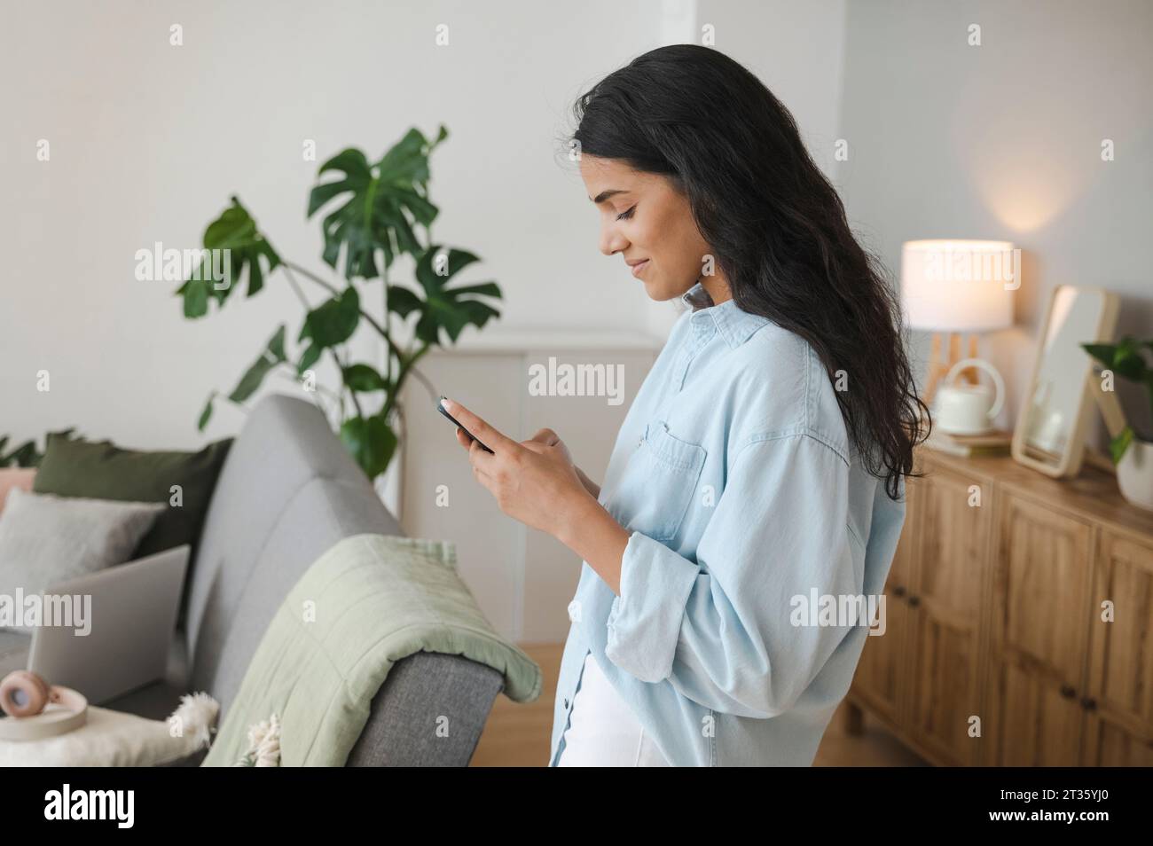Giovane donna che usa lo smartphone nel salotto di casa Foto Stock