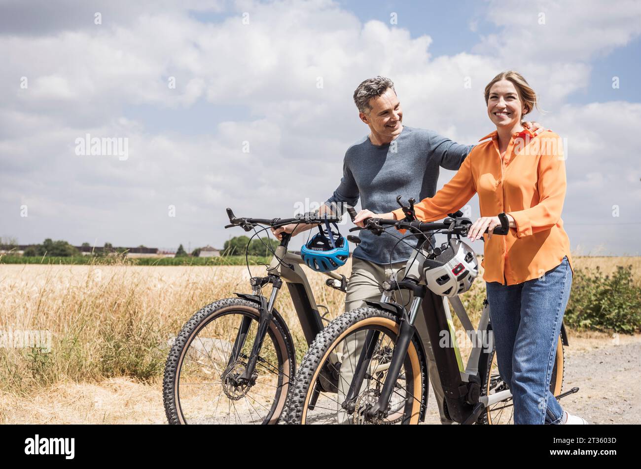 Una bella coppia che viaggia in bicicletta vicino al campo nelle giornate di sole Foto Stock