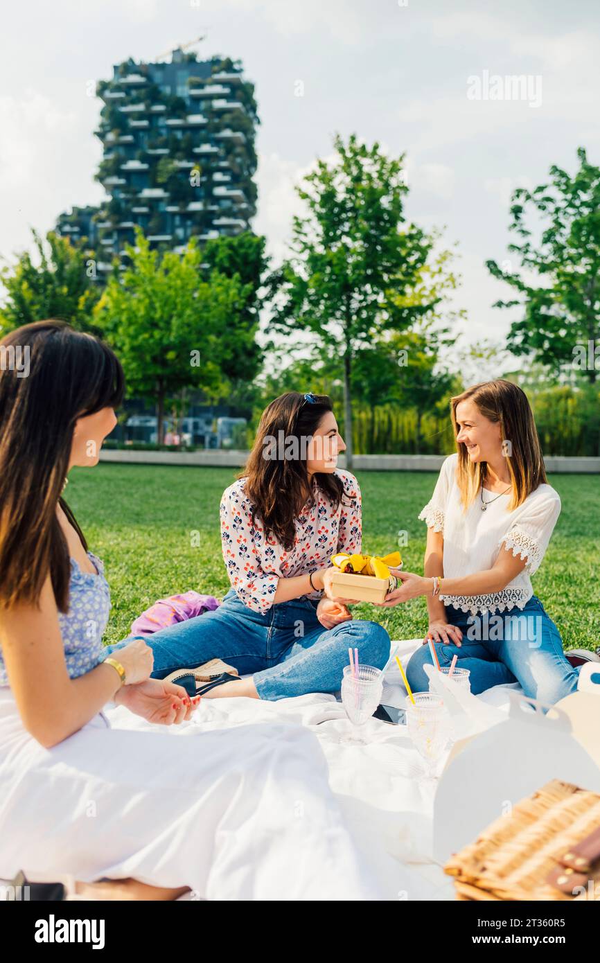 Donna felice con gli amici che tiene in mano una confezione regalo nella giornata di sole Foto Stock