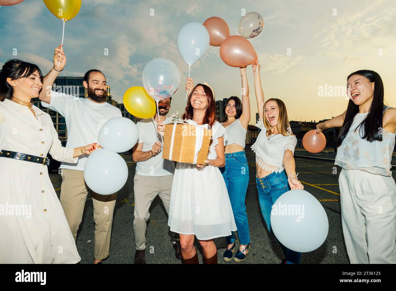 Amici allegri che festeggiano il compleanno della donna con palloncini e regali al tramonto Foto Stock