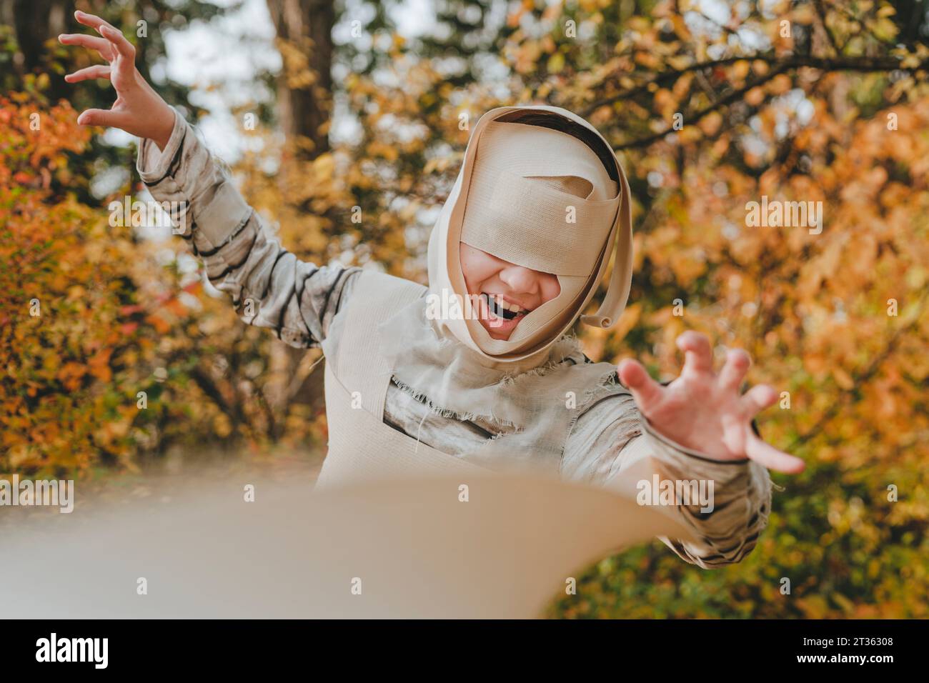 Ragazza gioiosa che indossa un costume da mummia e che si muove in giardino Foto Stock