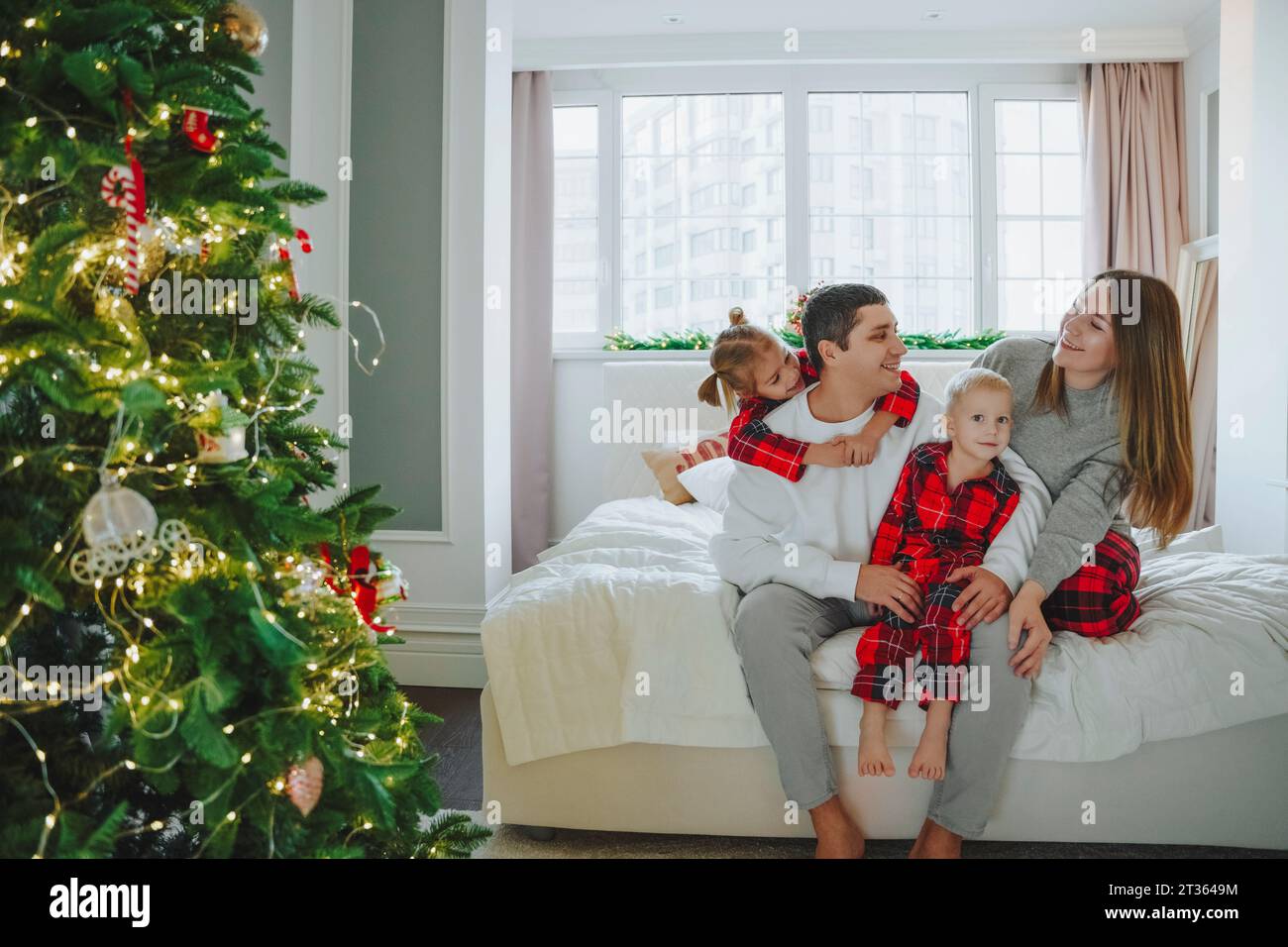 Famiglia seduta sul letto vicino all'albero di Natale a casa Foto Stock