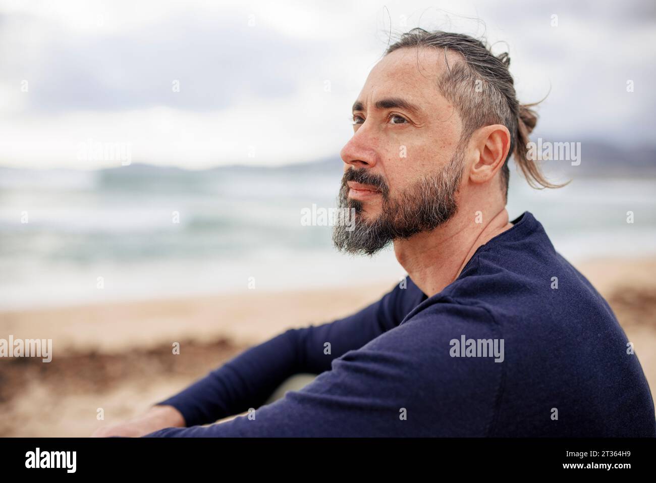 Uomo contemplativo che indossa una maglietta blu in spiaggia Foto Stock