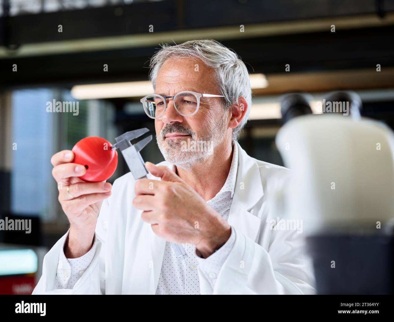 Scienziato che misura la sfera rossa con calibro in laboratorio Foto Stock