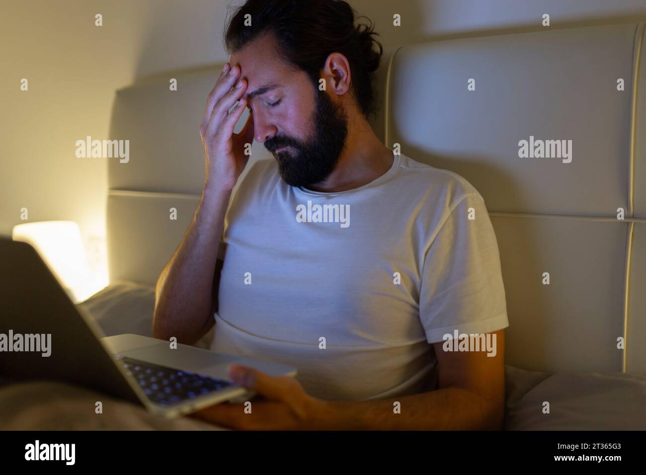Uomo con notebook che ha mal di testa a letto a casa Foto Stock