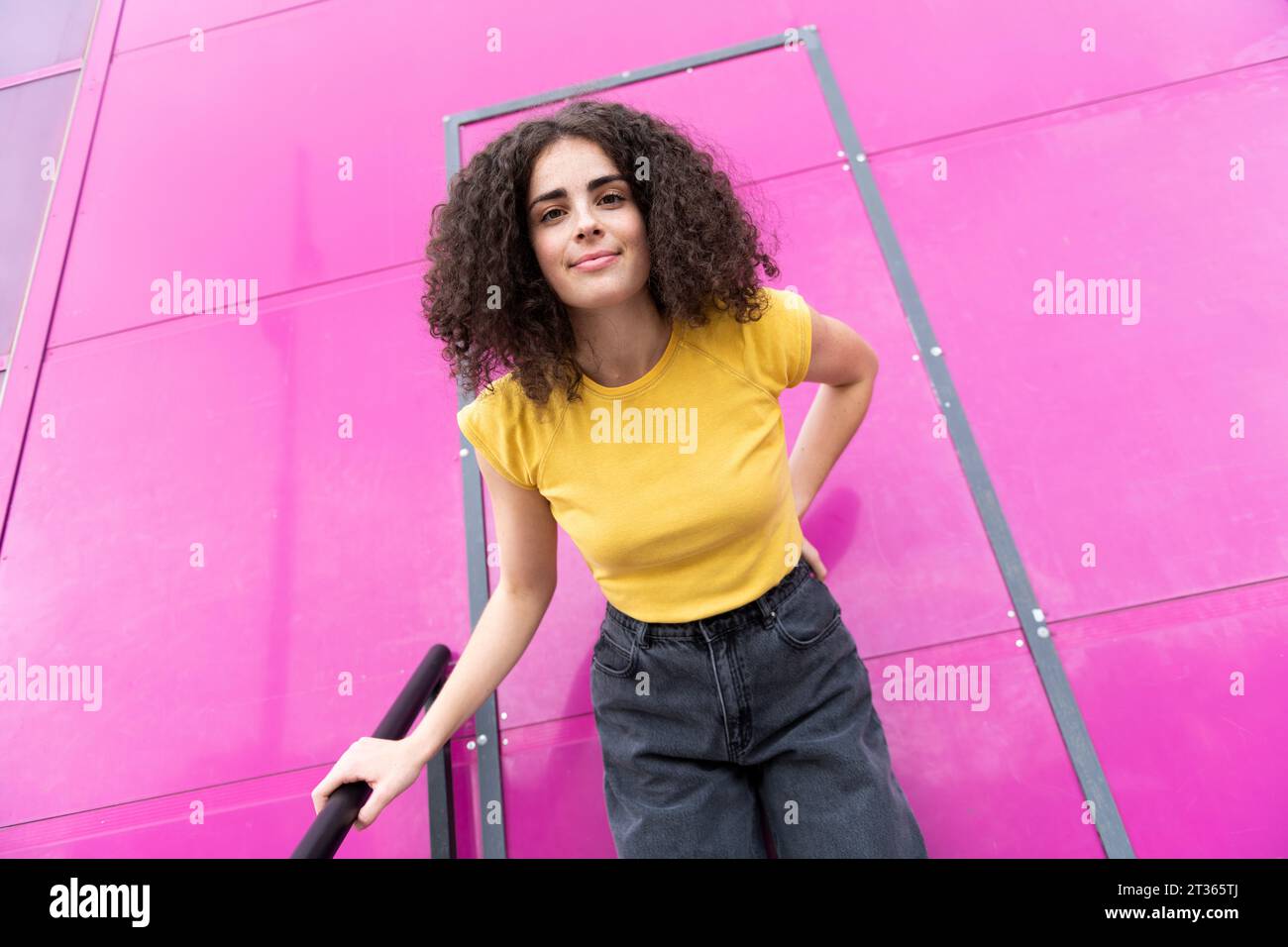 Donna sorridente con capelli ricci in piedi davanti alla porta rosa Foto Stock