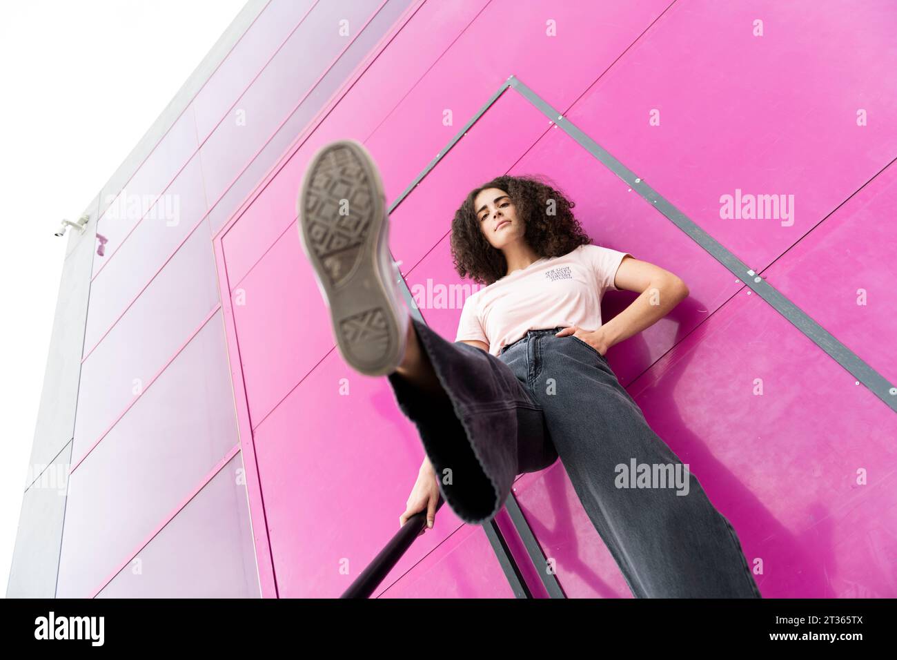 Giovane donna con la gamba in piedi davanti alla porta rosa Foto Stock