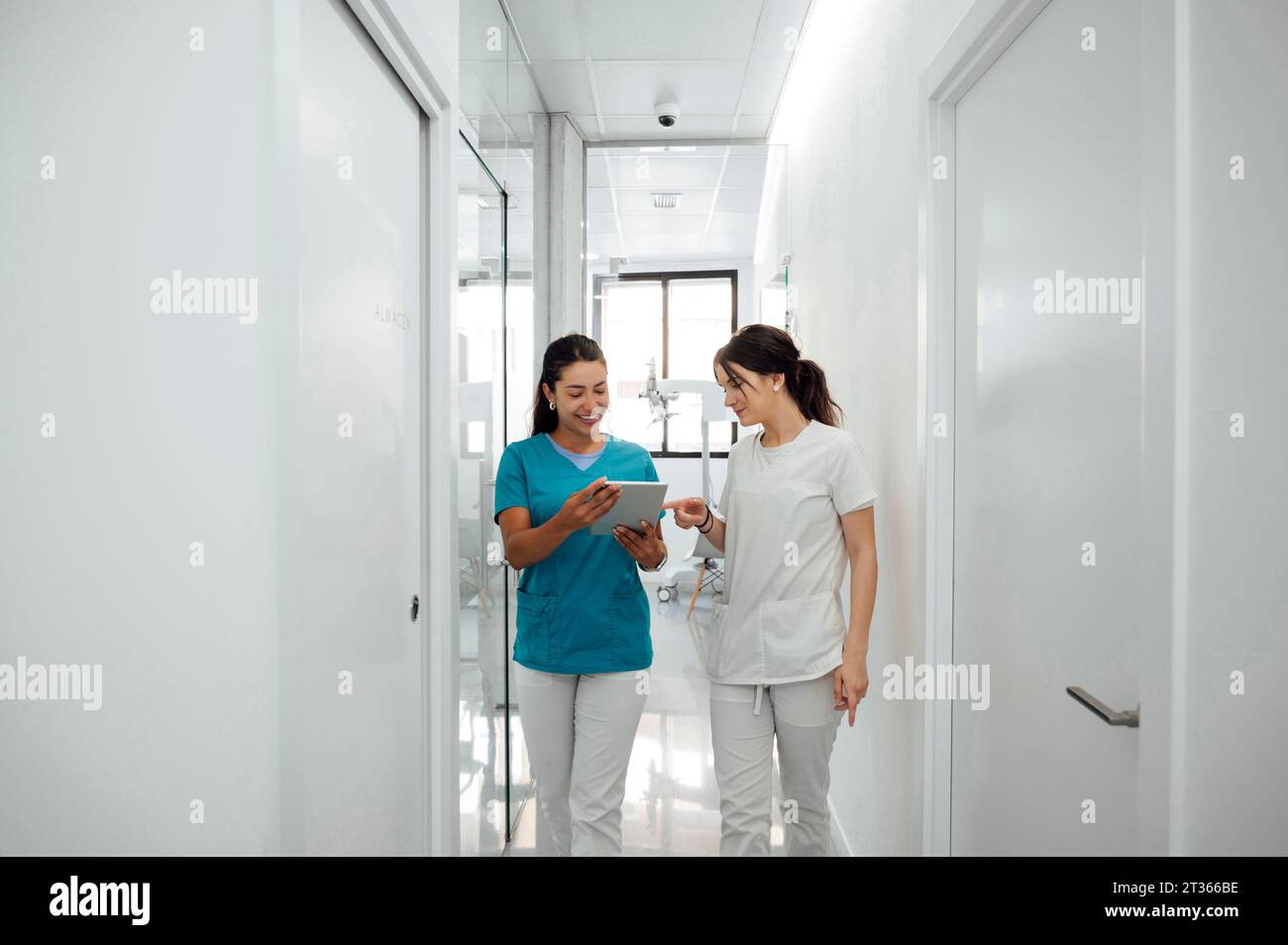 Felice dentista che discute con un collega su un tablet PC nel corridoio Foto Stock