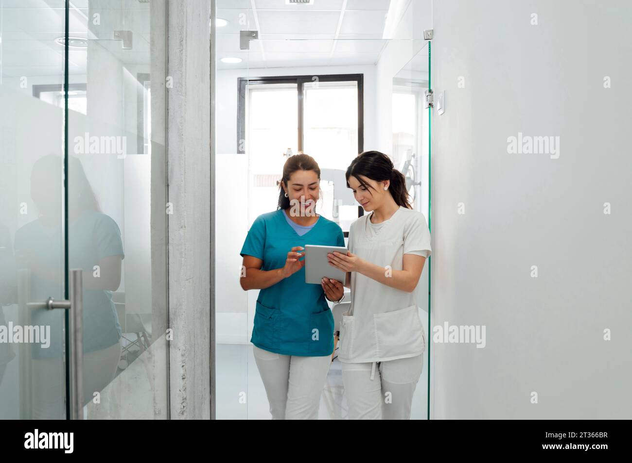 Dentista sorridente che discute con un collega su un tablet PC in clinica Foto Stock