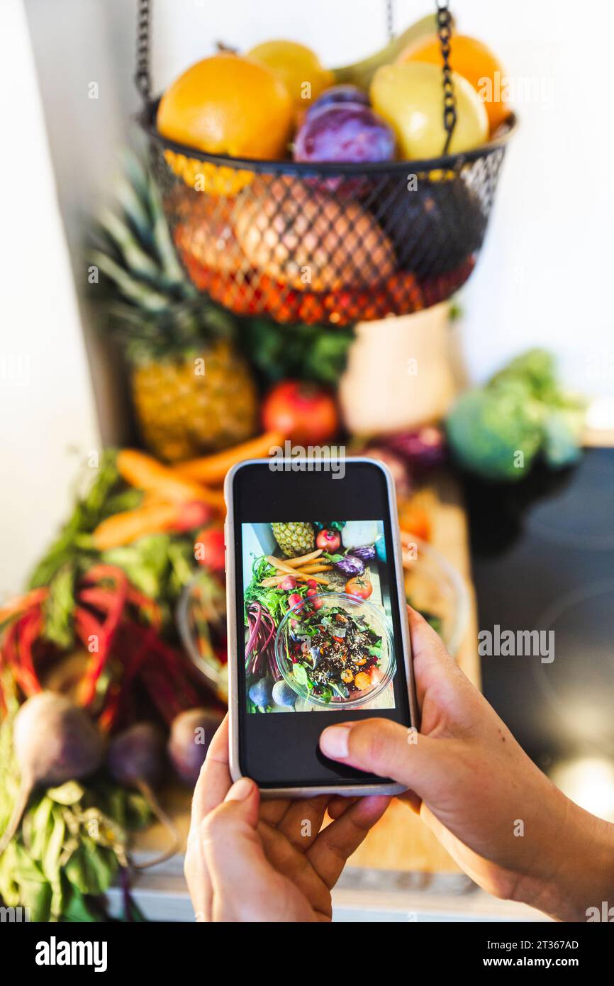 Mani di una donna che fotografa verdure e una ciotola di insalata in cucina a casa Foto Stock