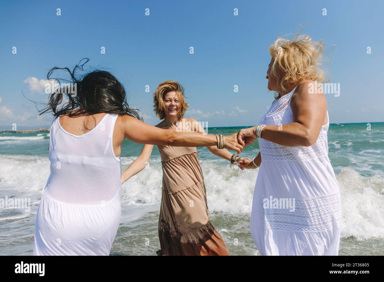 Donne felici che si divertono insieme vicino al mare ondulato in spiaggia Foto Stock