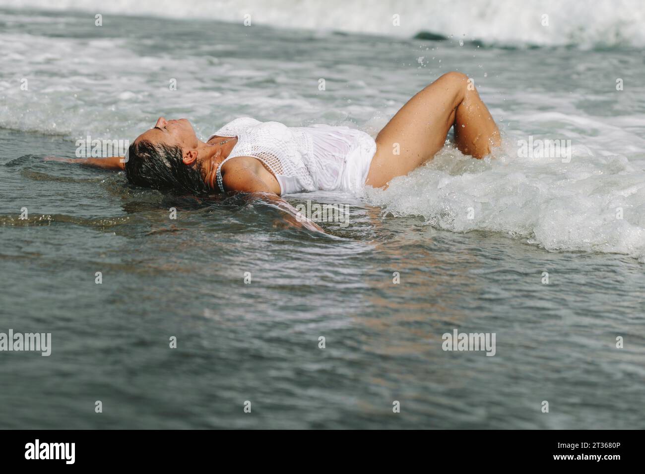 Donna sdraiata in mare ondulato in spiaggia Foto Stock