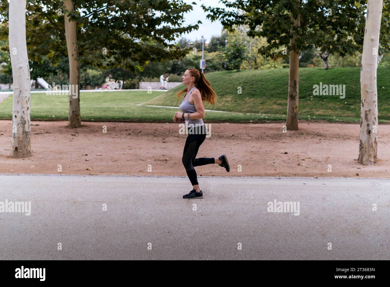 Redhead Woman che fa jogging sul sentiero del parco Foto Stock