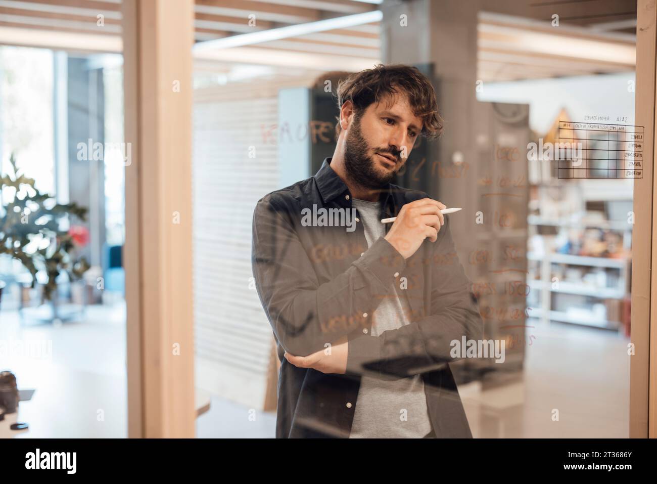 Un uomo d'affari premuroso che scrive su una parete di vetro in ufficio Foto Stock