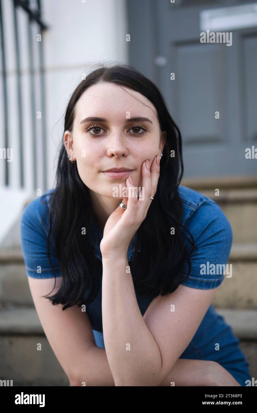 Giovane donna sorridente seduta su gradini Foto Stock