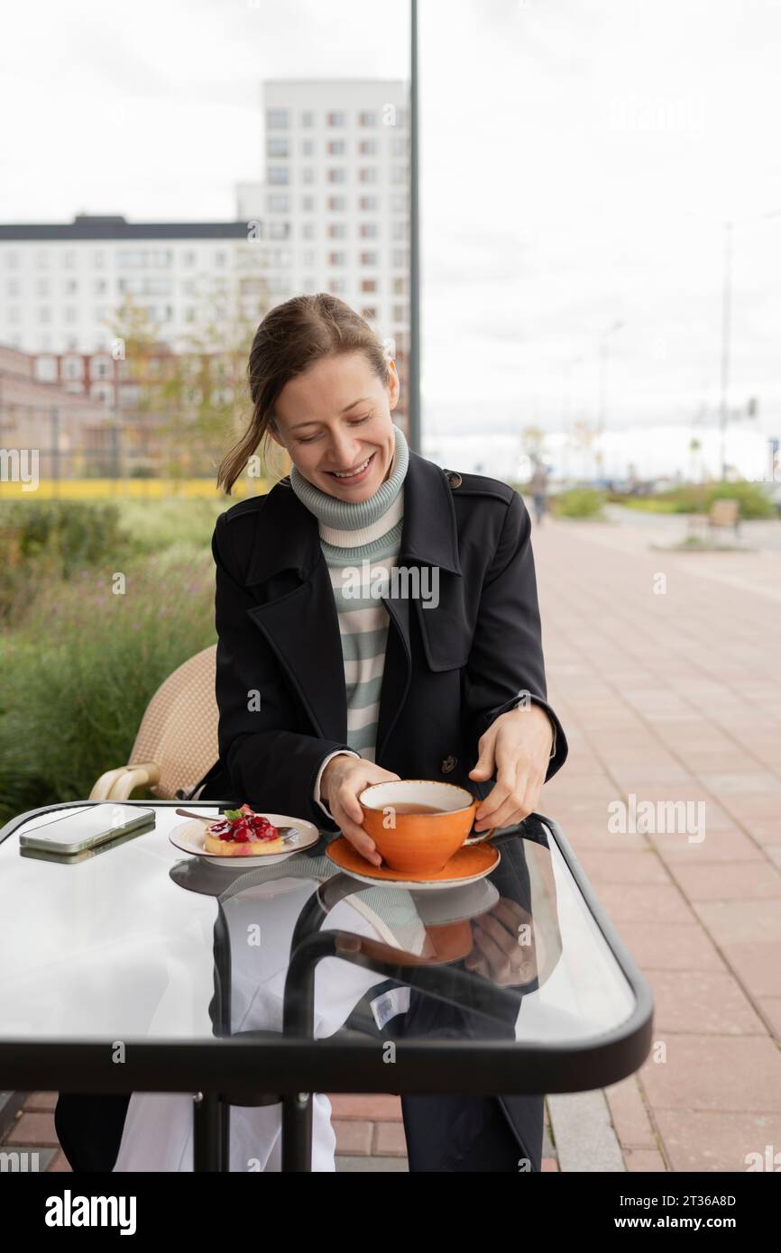 Donna sorridente che tiene una tazza di tè al caffè del marciapiede Foto Stock