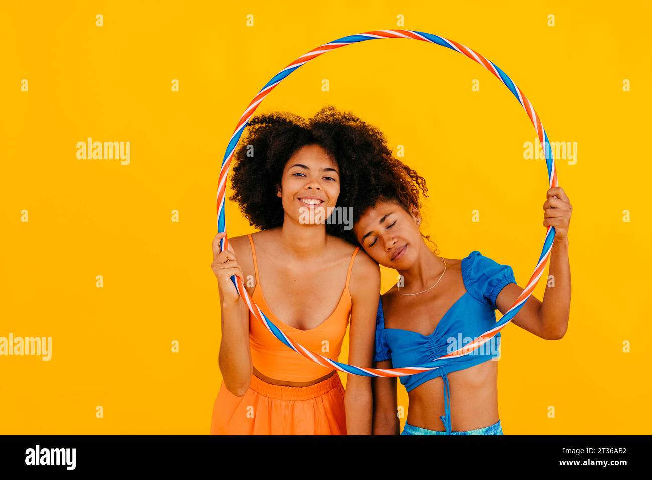 Donna addossata ad un amico che tiene un cerchio di plastica su sfondo giallo Foto Stock