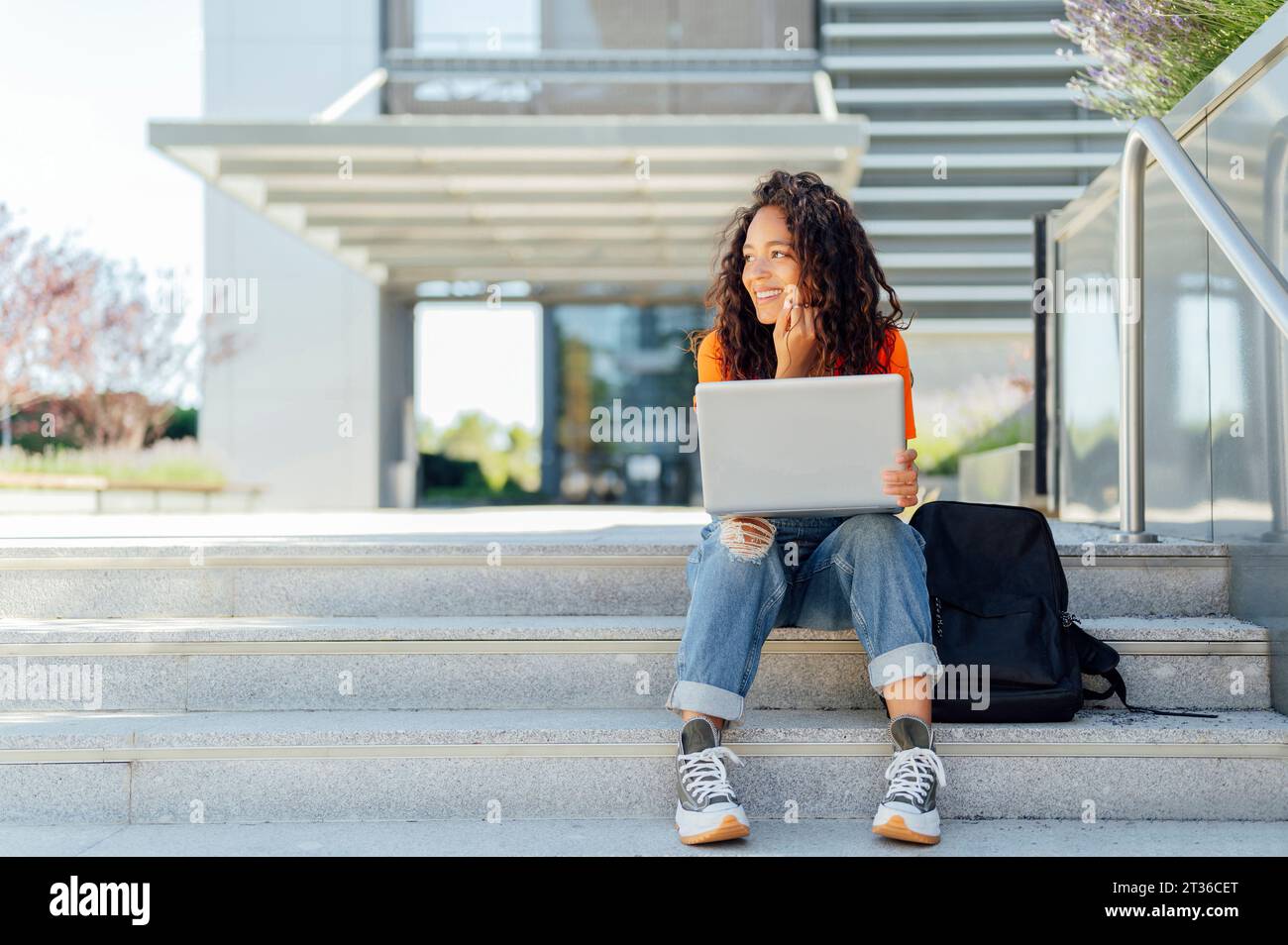 Studente sorridente seduto con un notebook sui gradini del campus Foto Stock
