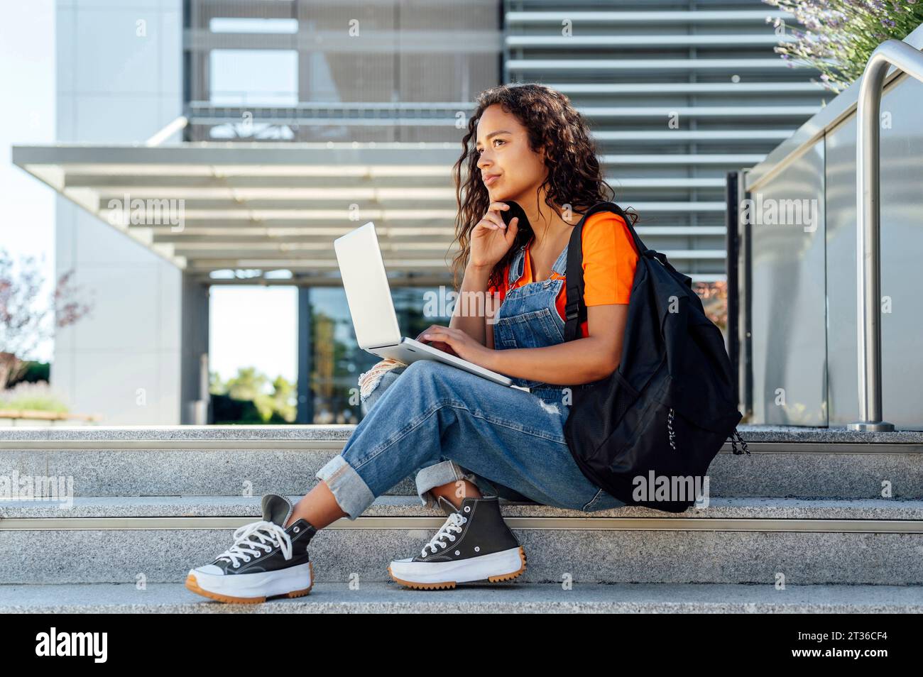 Studente contemplativo seduto con notebook sui gradini del campus Foto Stock