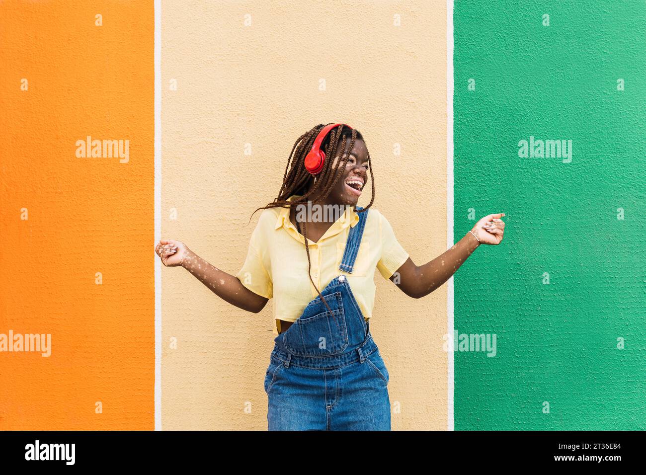 Giovane donna felice che balla di fronte a una parete multicolore Foto Stock
