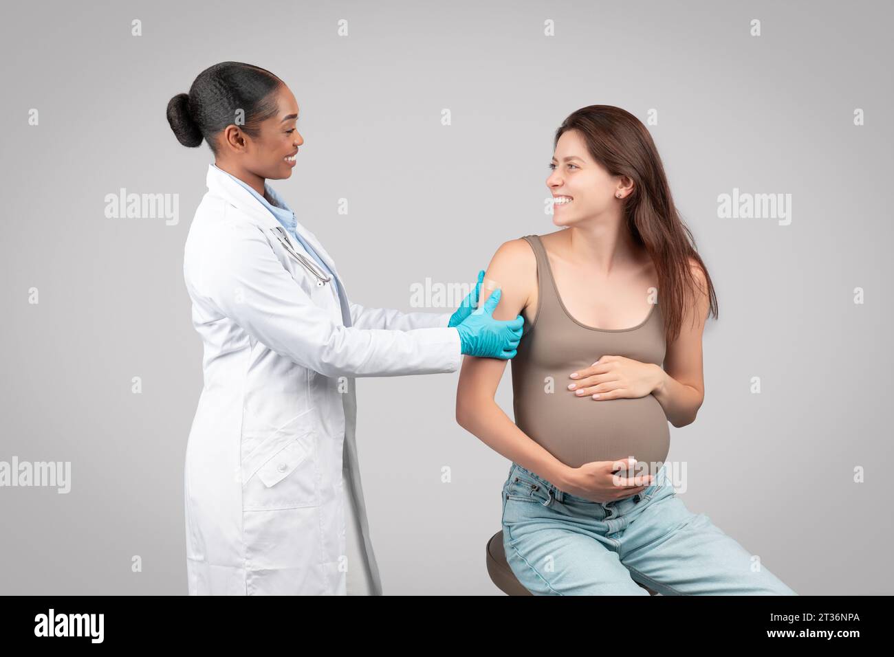 Allegro medico donna nera fare iniezione a paziente incinta durante la gravidanza, mette gesso a portata di mano Foto Stock