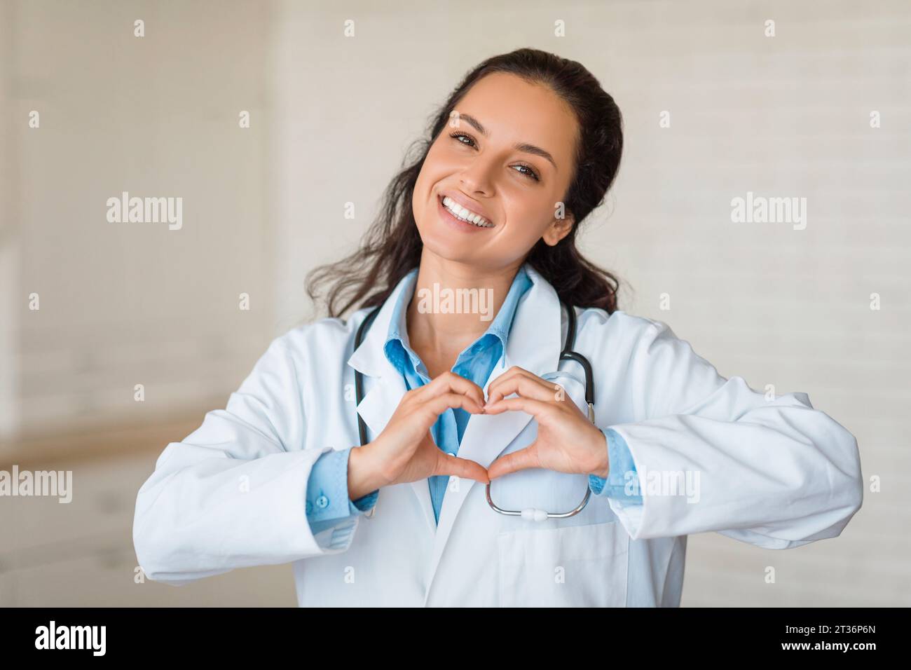 Medico allegro che crea forma a cuore con le mani, sorridendo alla macchina fotografica Foto Stock