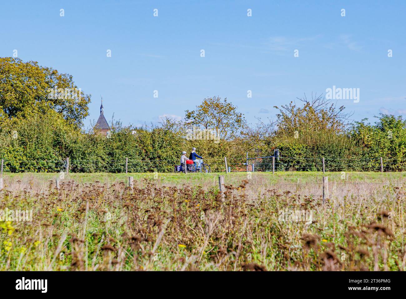 Meers, Elsloo, Paesi Bassi. 24 settembre 2023. Paesaggio rurale olandese con due ciclisti in bicicletta su una pista ciclabile tra terreni agricoli, cespugli, coira Foto Stock