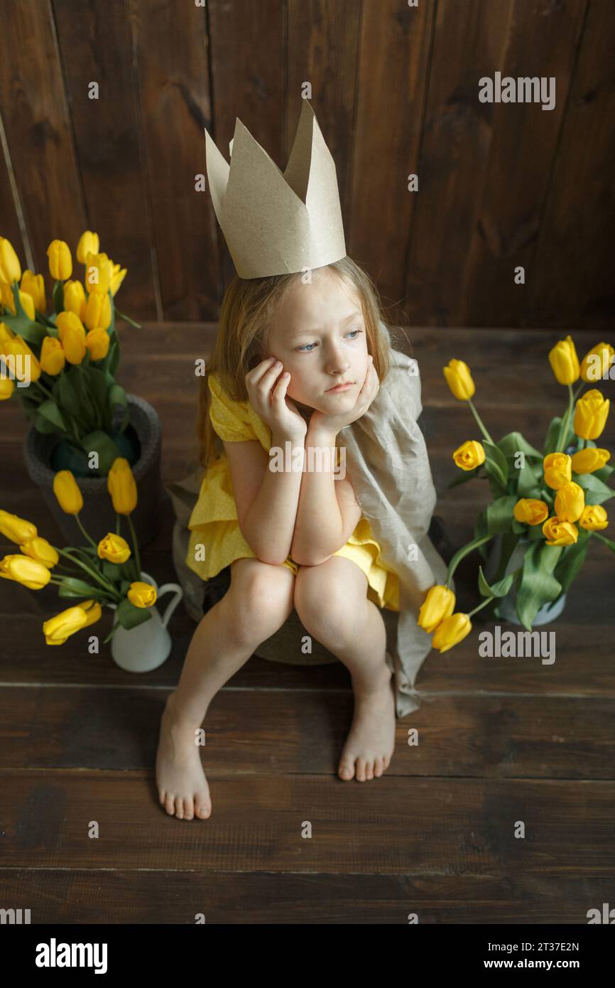 Ritratto di una triste principessa seduta accanto a mazzi di tulipani gialli. Siede triste, pensando. Telaio verticale. Foto Stock