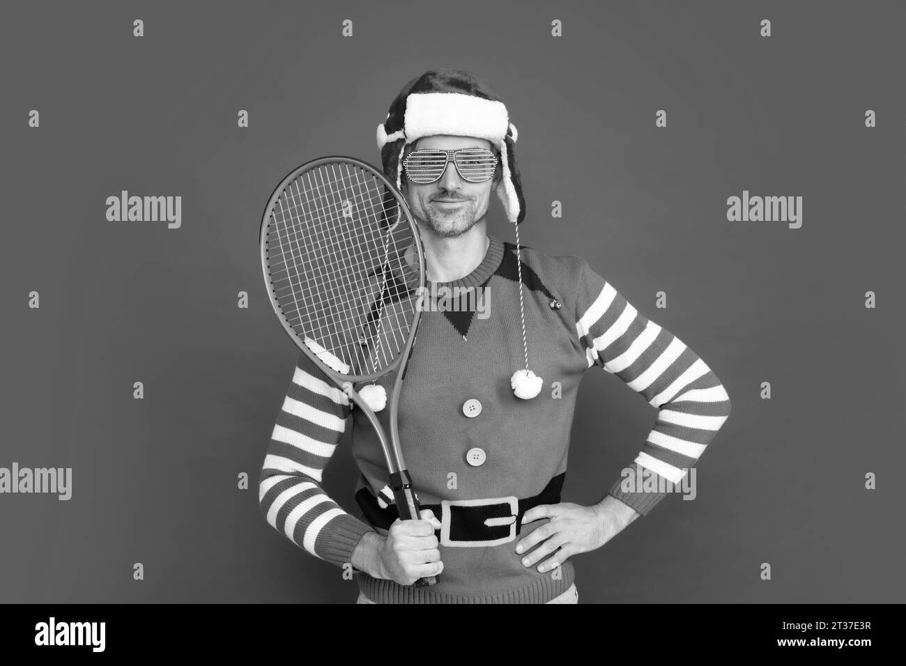 un allegro ragazzo di natale tiene il razzo da tennis su sfondo rosso. felice anno nuovo. buon natale. uomo in costume da elfo e cappello di babbo natale. Foto Stock