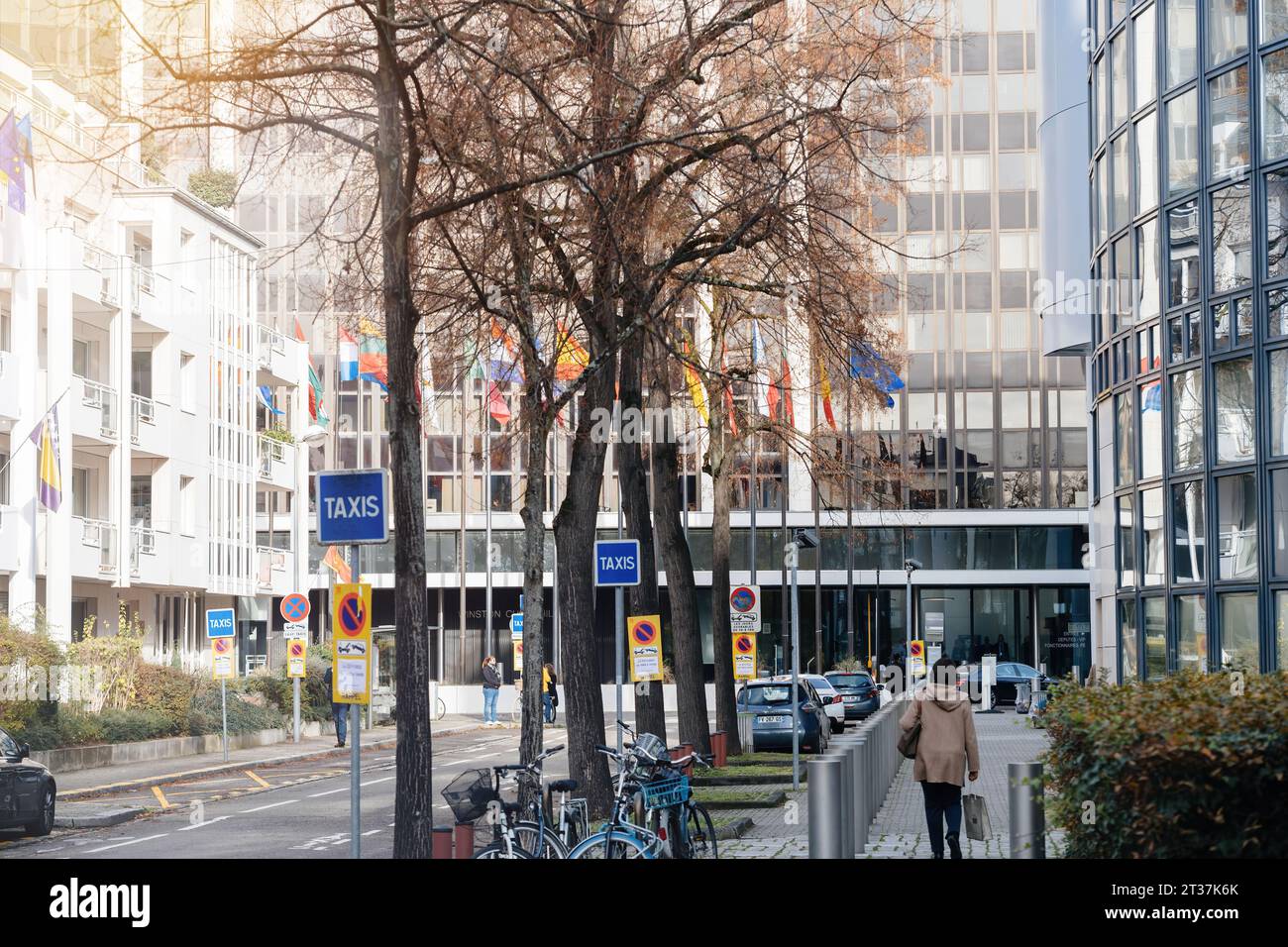 Strasburgo, Francia - 22 novembre 2023: Lungo la strada è presente un cartello taxi, con sullo sfondo l'edificio Winston Churchill del Parlamento europeo. Una donna pedonale può essere vista camminare nelle vicinanze, aggiungendo vita alla scena urbana Foto Stock