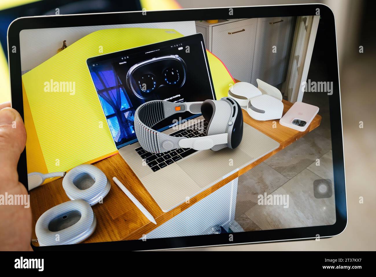 Parigi, Francia - 6 giugno 2023: Un'immagine su un tablet iPad mostra una scrivania in legno con un laptop che mostra futuristici occhiali Vision Pro, un visore VR a righe appoggiato sulla tastiera, accessori per cuscinetti auricolari abbinati, uno stilo e uno smartphone rosa Foto Stock
