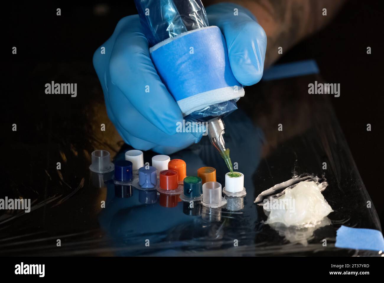 La mano con i guanti del tatuatore mescola l'ago in colori verde e bianco per mescolare. Foto Stock