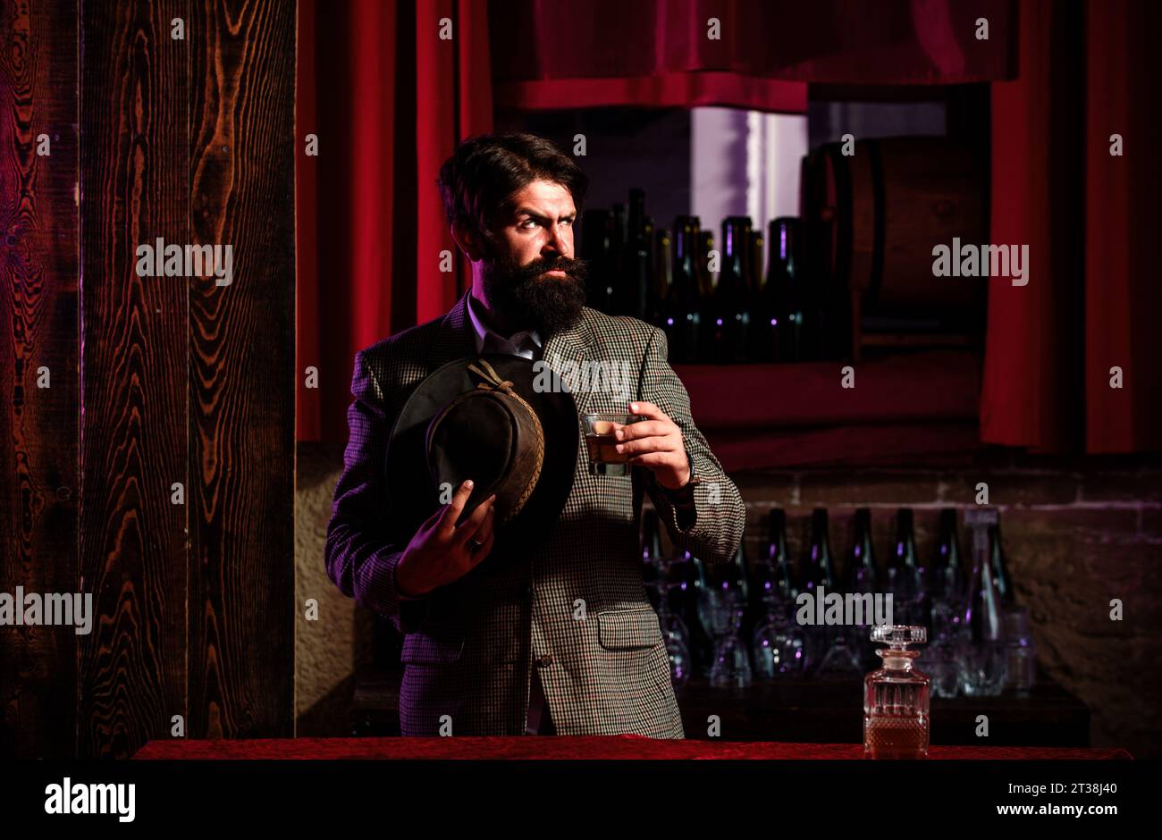 Uomo serio con un bicchiere di brandy. Uomo lavoratore vintage con barba lunga che tiene il whiskey. Seduto al bar. Foto Stock