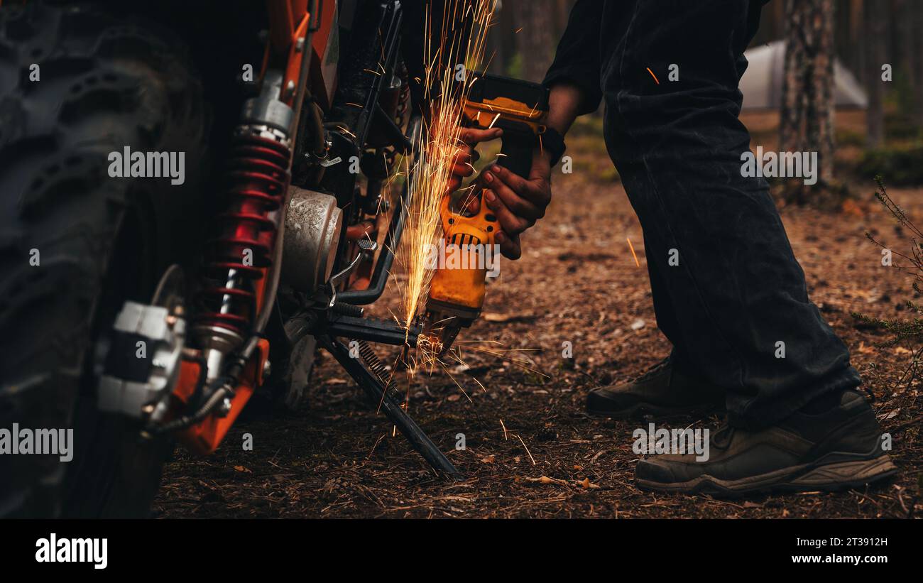 il meccanico maschile ripara una motocicletta personalizzata con una smerigliatrice Foto Stock