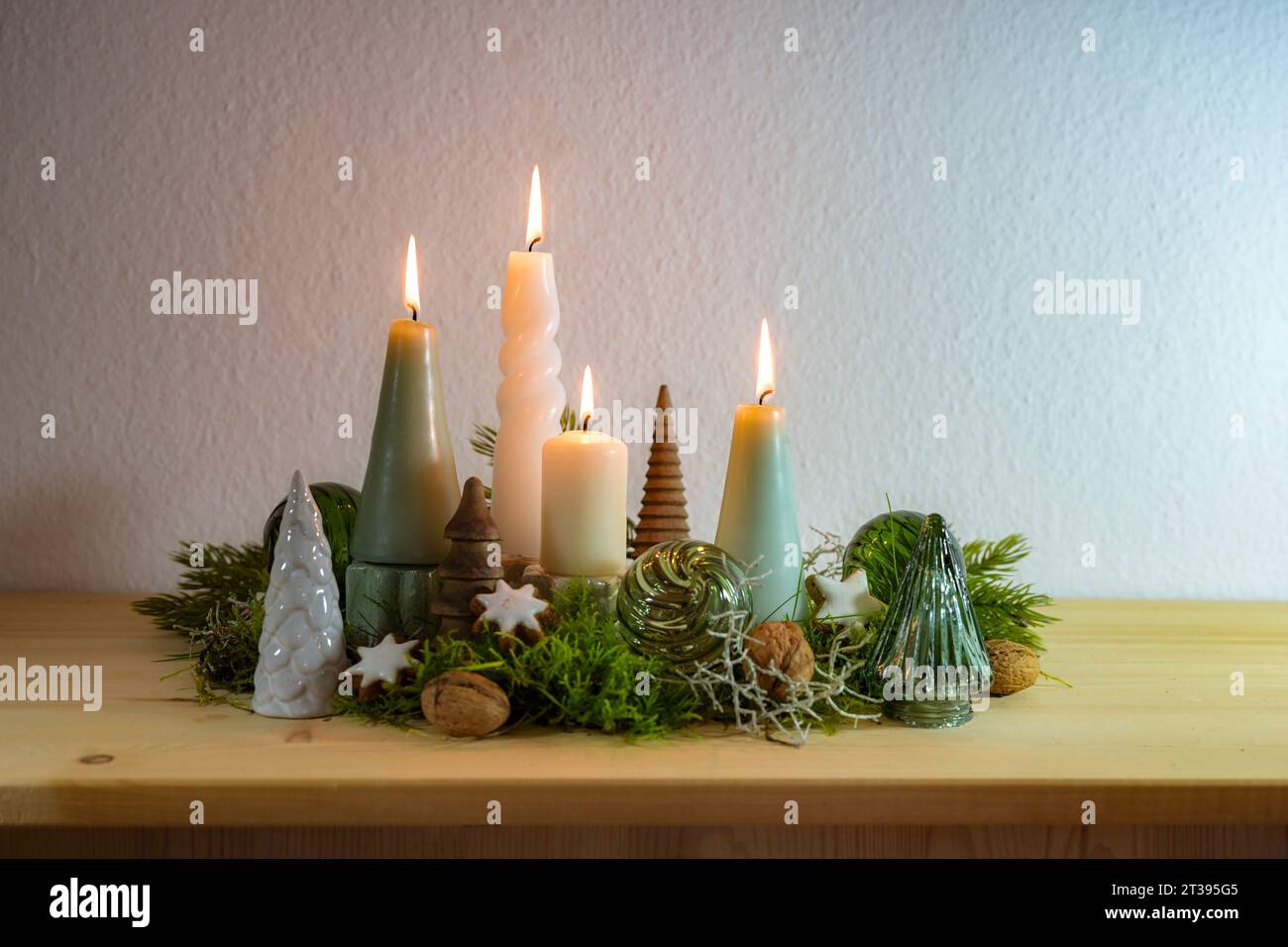Quarto Avvento, decorazione con quattro diverse candele accese, alcuni muschi, palline di Natale verdi di vetro e stelle di cannella su una credenza di legno agains Foto Stock