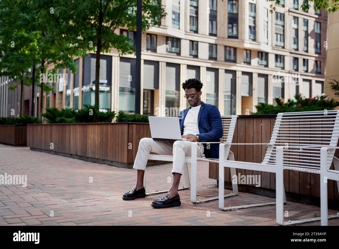 Uomo di colore con computer portatile che lavora in strada vicino al business center della città. Uomo d'affari alla moda all'aperto. Foto Stock
