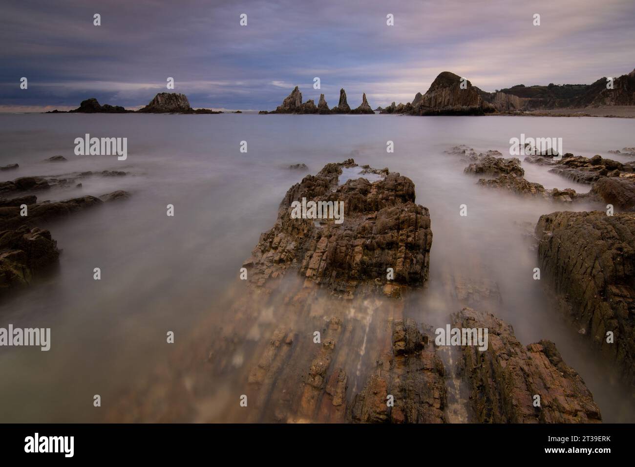 Foto di una spiaggia tranquilla al crepuscolo, con rocce nell'acqua che creano un bellissimo effetto di esposizione lunga Foto Stock