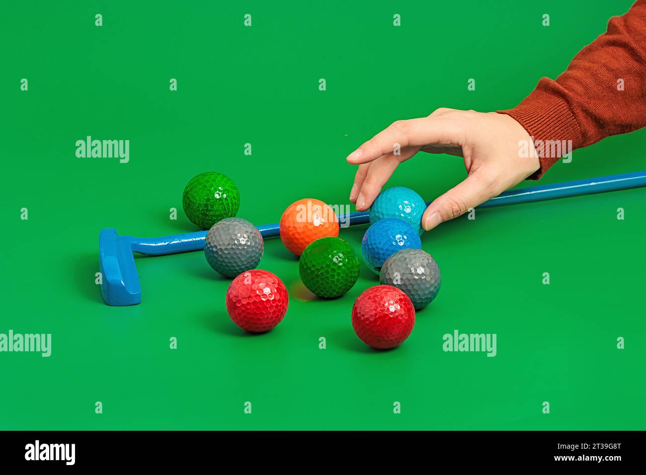 Ritaglia la palla con la mano nel campo da minigolf su una superficie verde in studio con bastoncino da golf e con varie palle Foto Stock