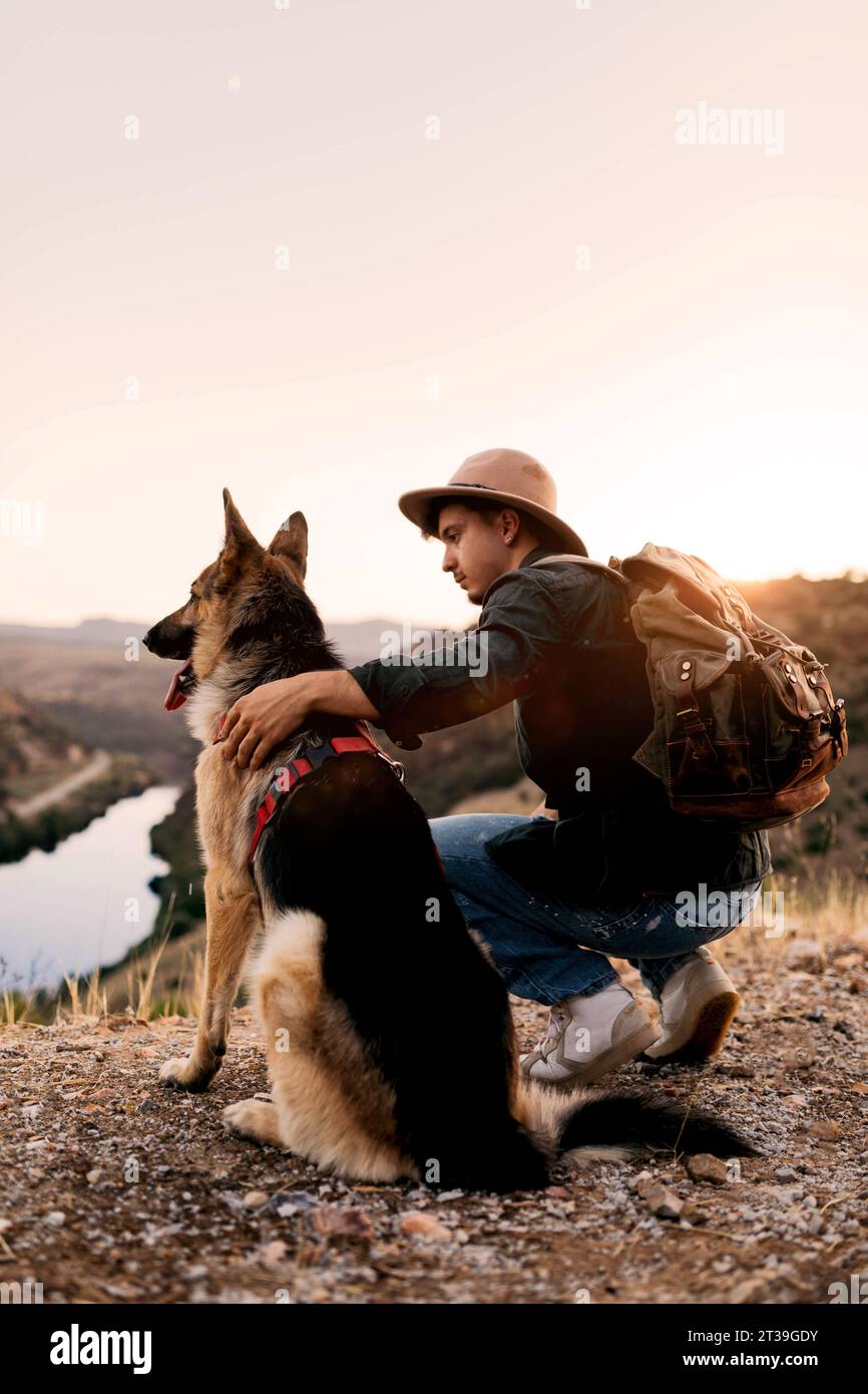 Vista laterale dell'amichevole cane pastore tedesco con un uomo seduto nella natura nelle giornate di sole durante una passeggiata nella natura Foto Stock